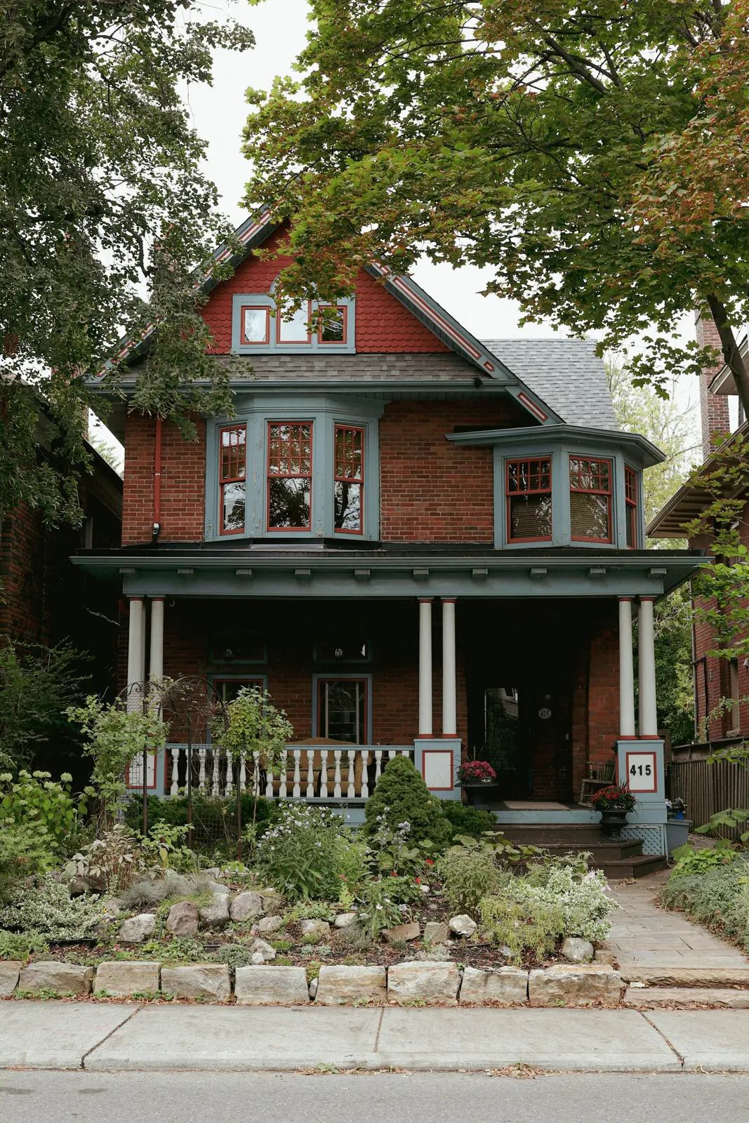 Red brick house with a wide front porch on a Toronto street